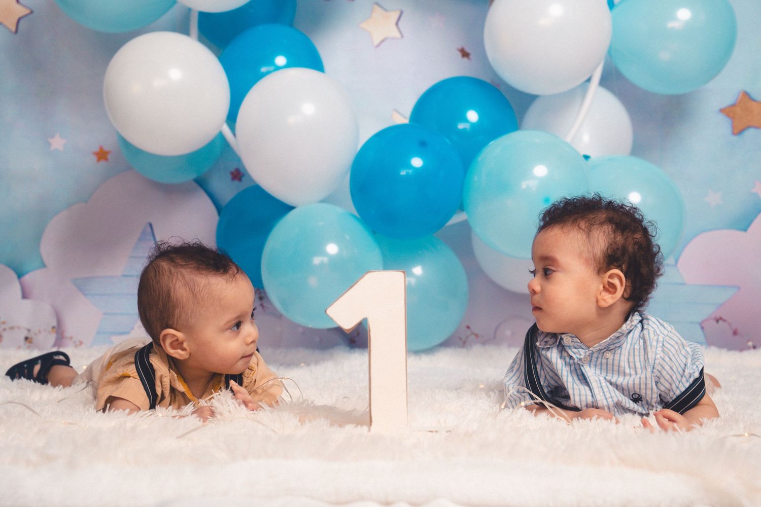 Baby crawling on white surface with blue and white balloons overhead.