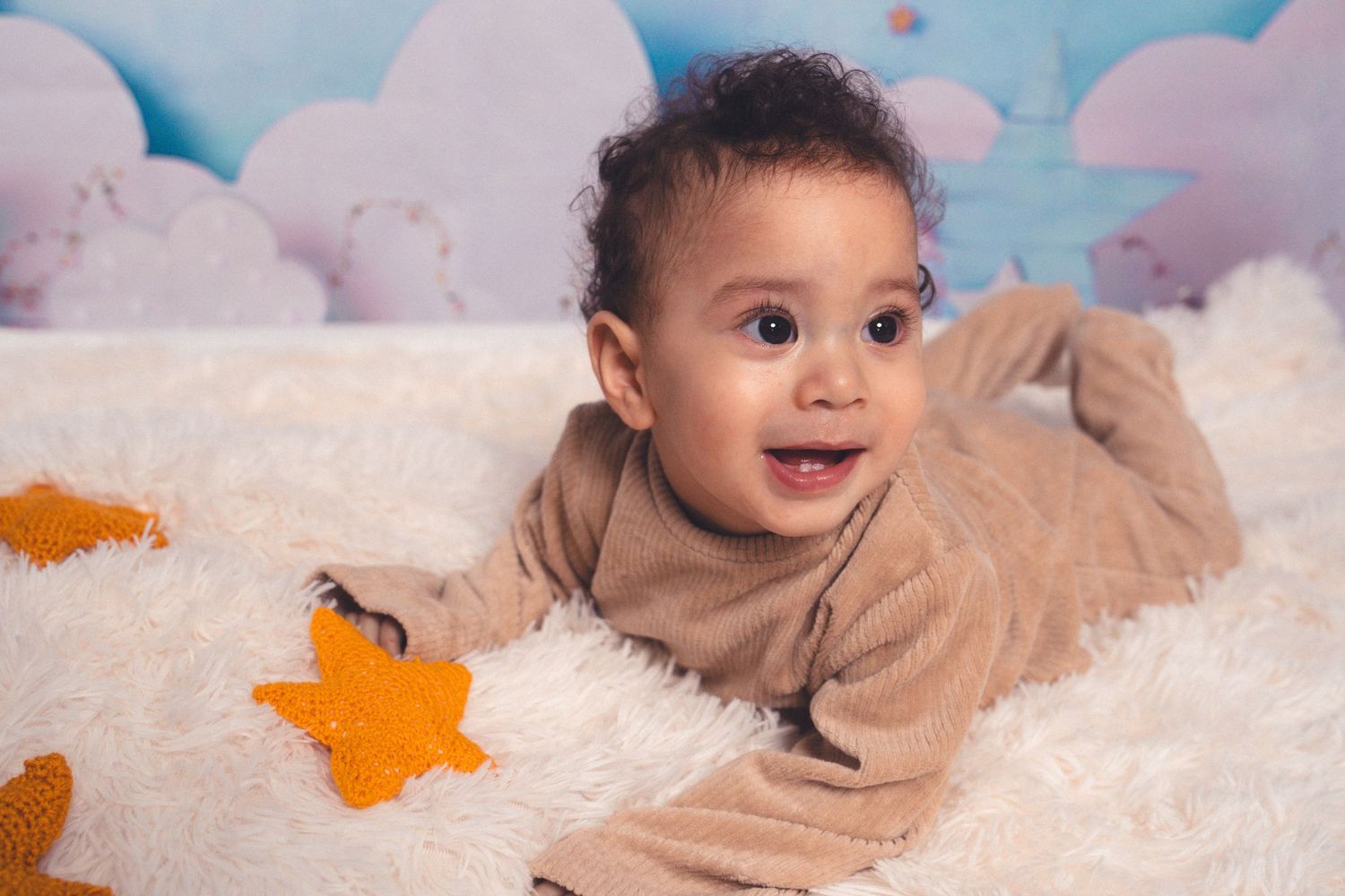Baby photoshoot setup with brown outfit against white backdrop and blue balloons.