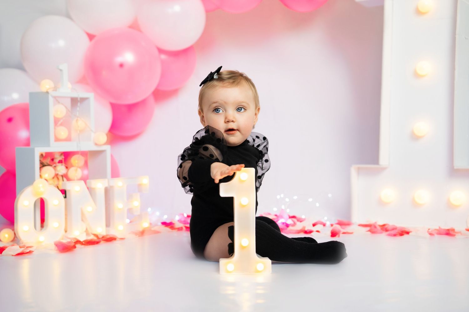 First birthday photoshoot with pink balloons and illuminated number one decoration.