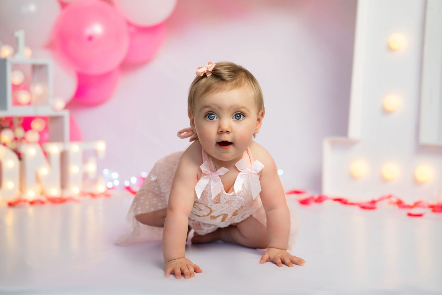 Baby photoshoot with pink balloons and twinkling lights in a dreamy setting.