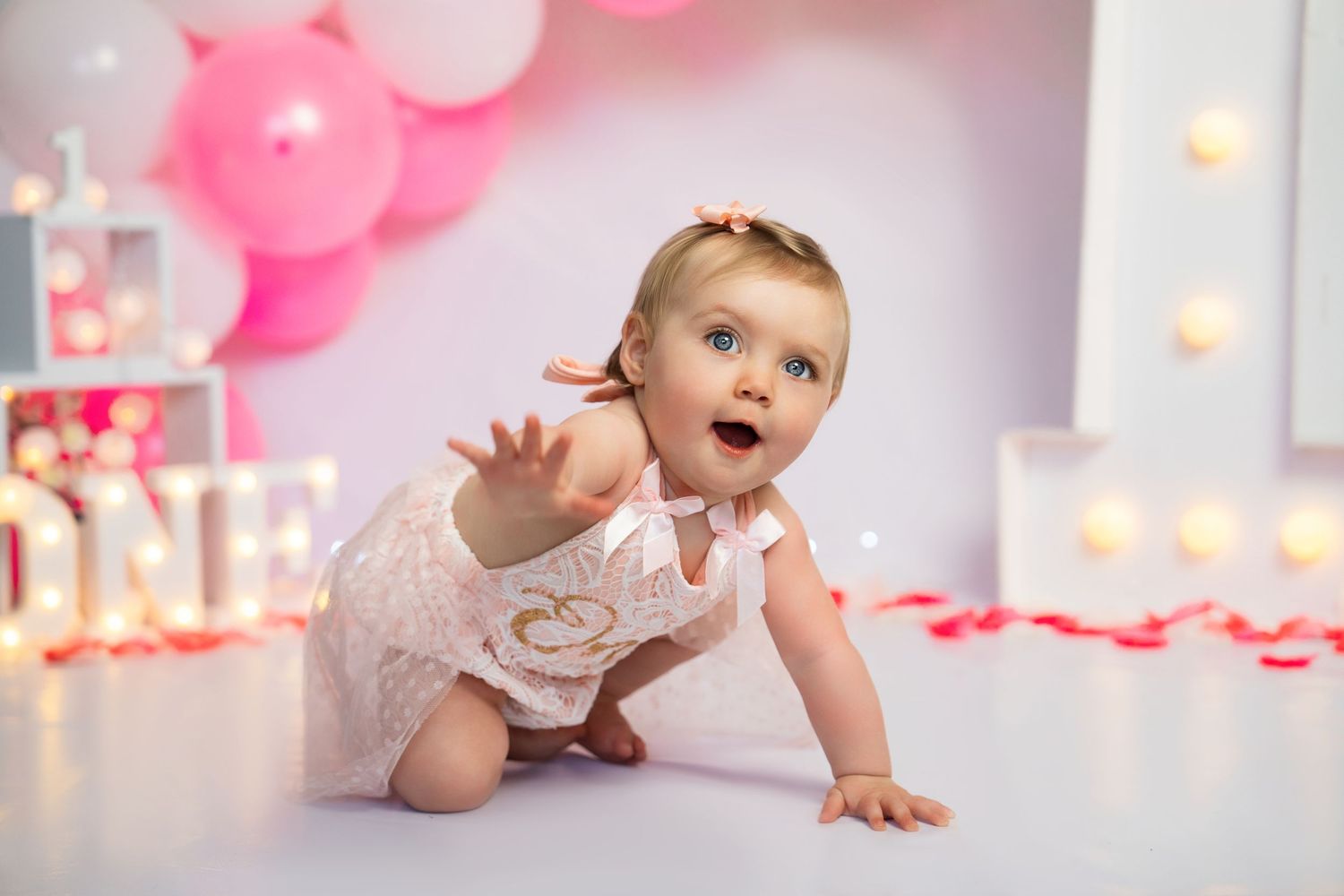 Baby crawling and smiling during a pink-themed photoshoot with fairy lights.