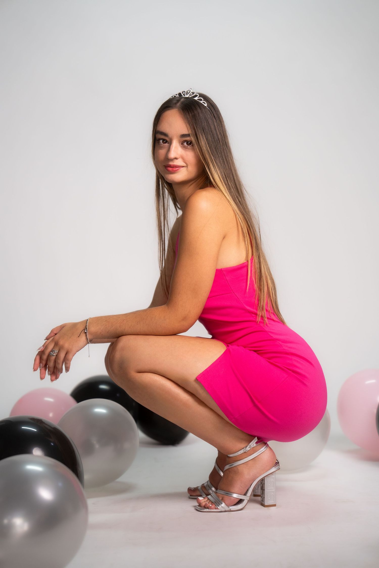 Model in hot pink dress poses with black and pink balloons against white backdrop for a photo series.