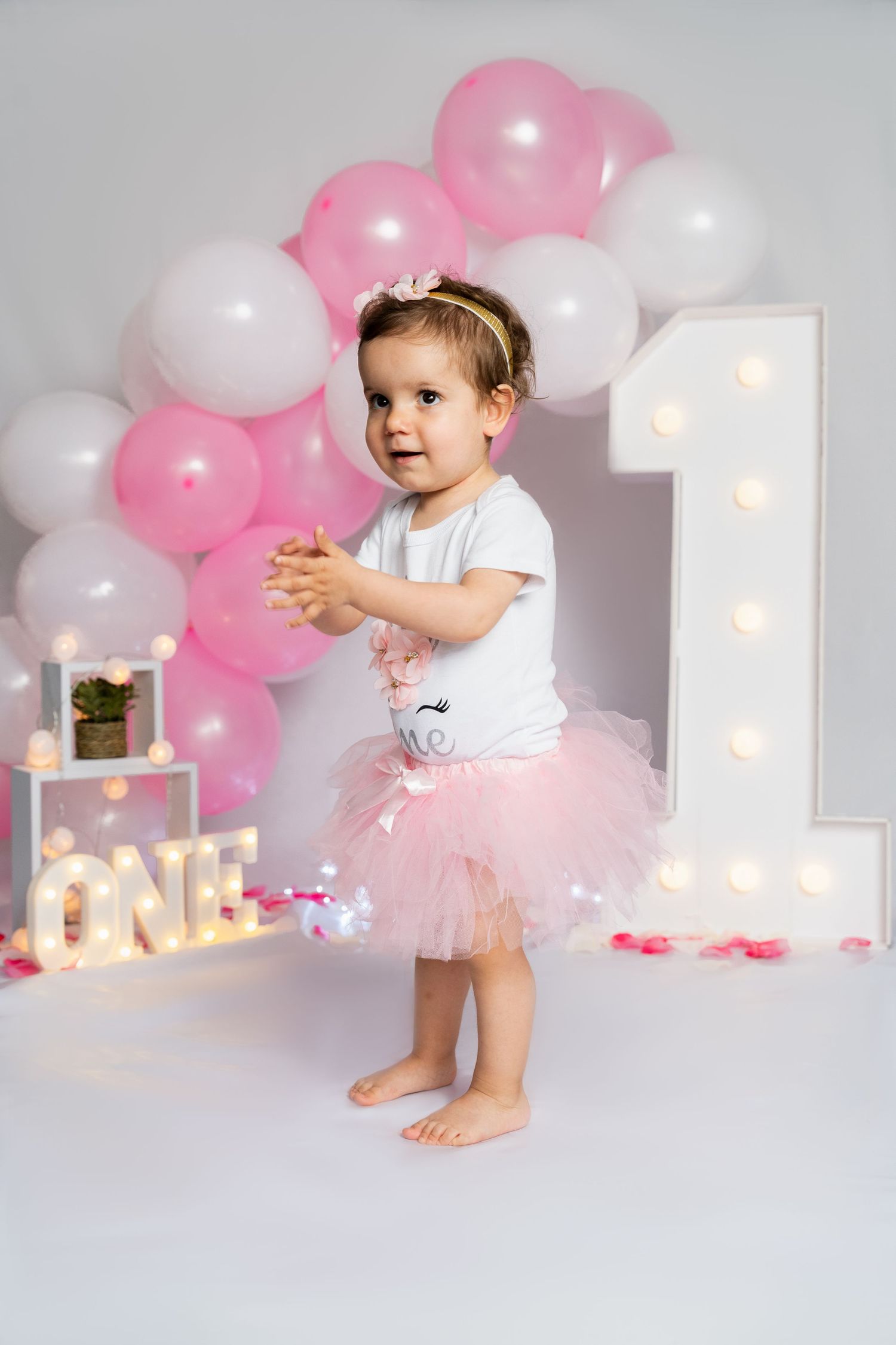 Birthday photoshoot with pink balloon arch and illuminated number one decoration.