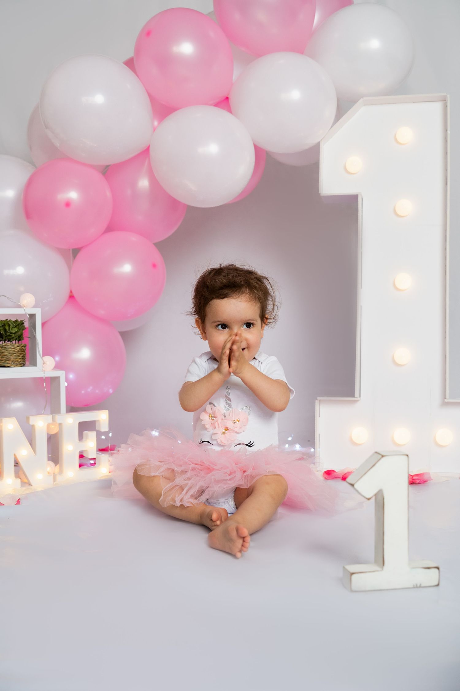 First birthday celebration setup with pink balloons and lit number one sign.
