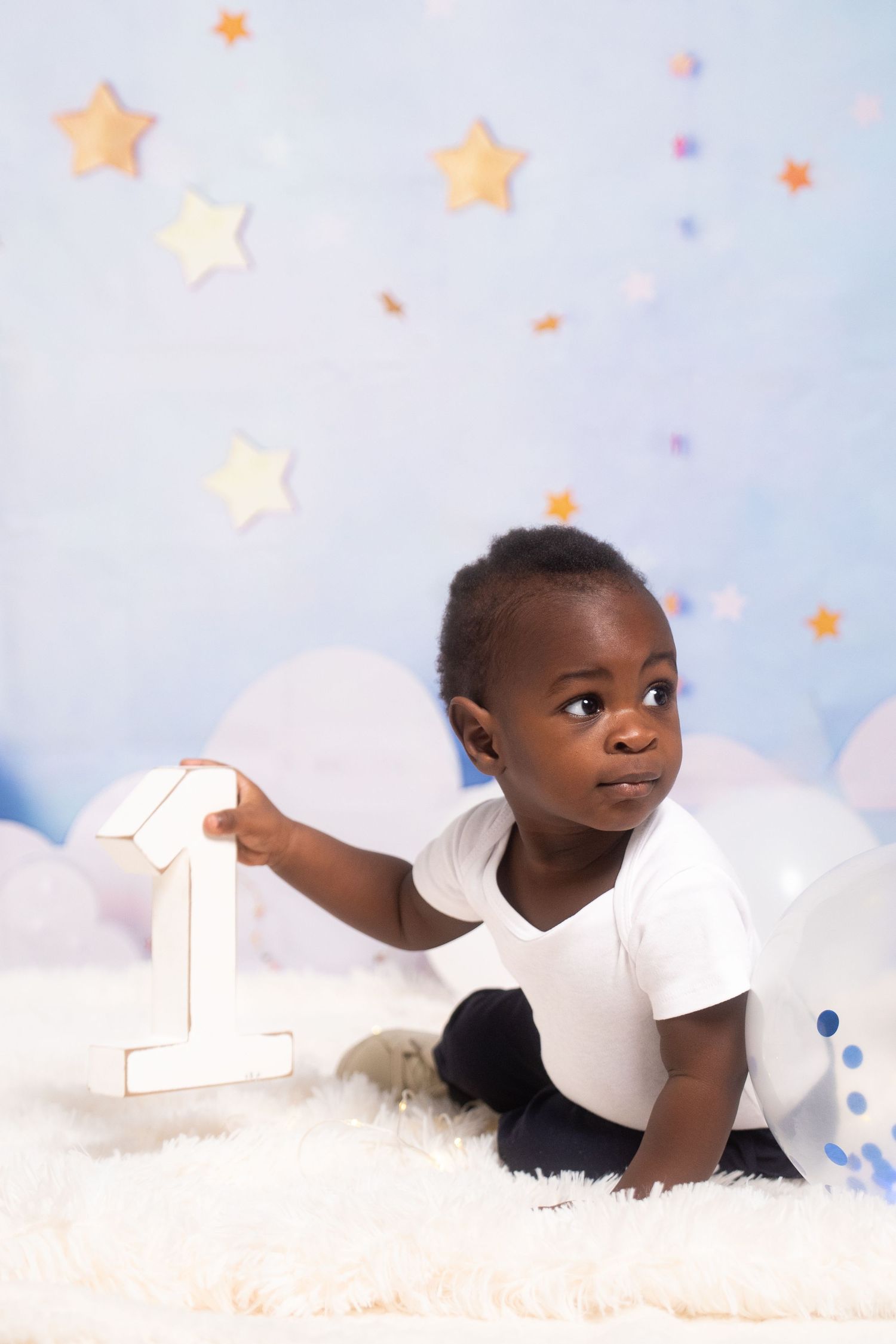 Baby in white outfit lying on fluffy white surface with star decorations.