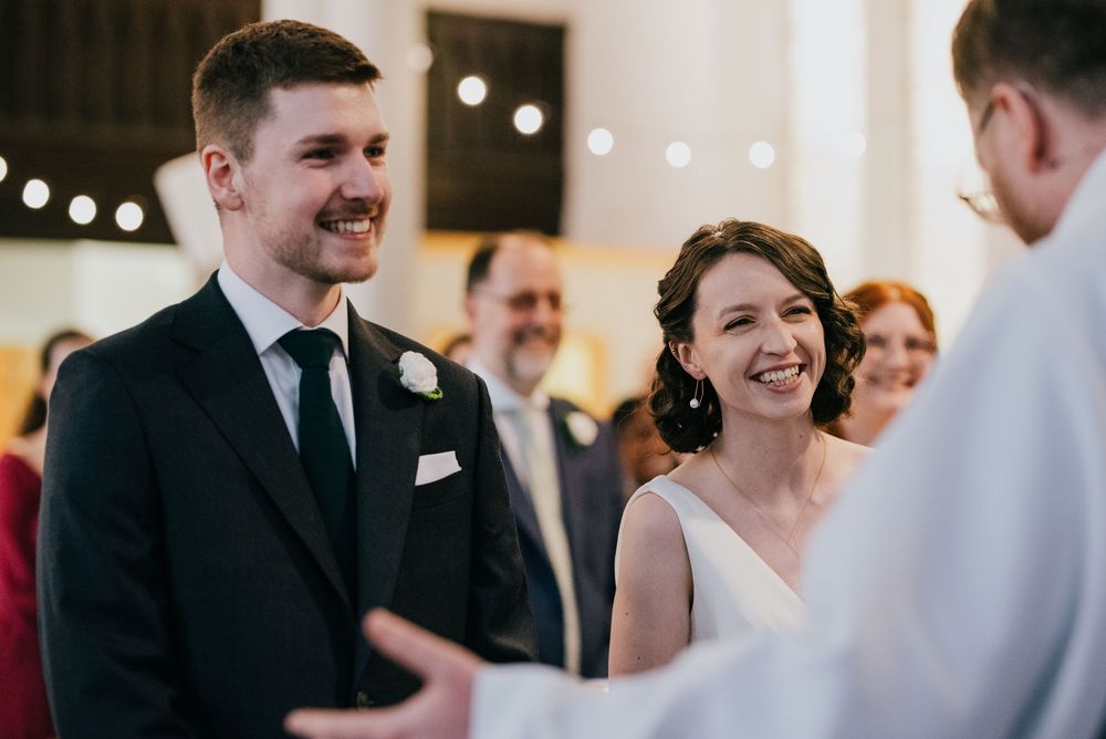 A couple exchanges vows during their wedding ceremony while surrounded by loved ones and soft lighting.