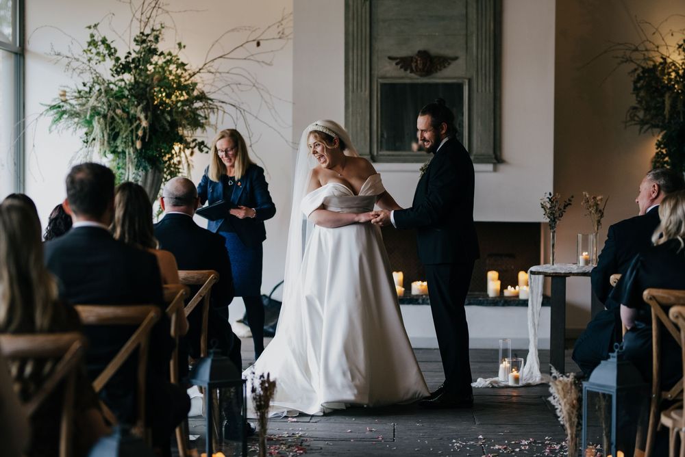 A wedding ceremony taking place in an elegant indoor venue with wooden chairs and floral decor.
