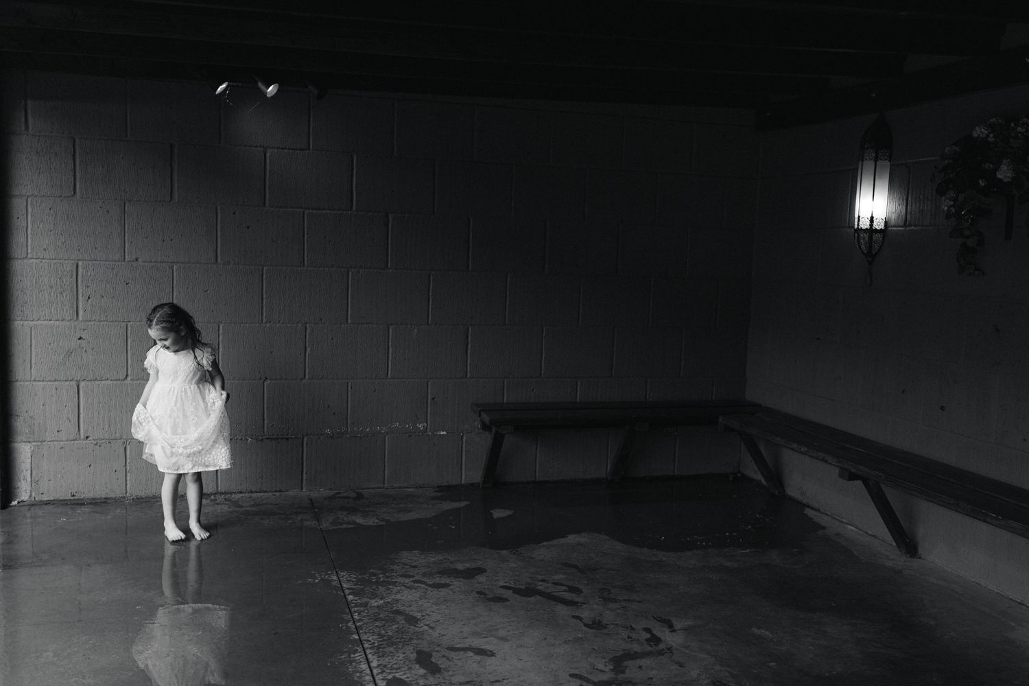 A lone figure in white stands against a dark wall in dramatic black and white.