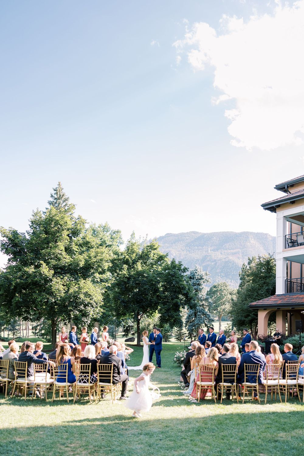 Outdoor wedding ceremony setup with wooden chairs on grass against mountain backdrop.