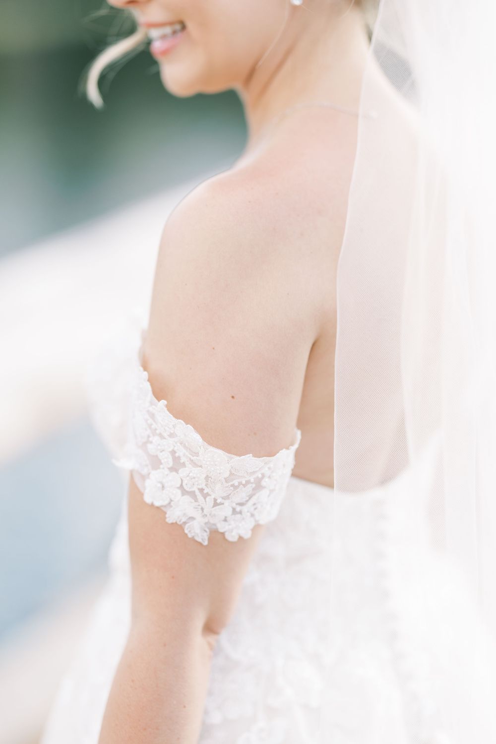 Close up of delicate white lace details on the arm and bodice of an ethereal wedding dress with a veil.