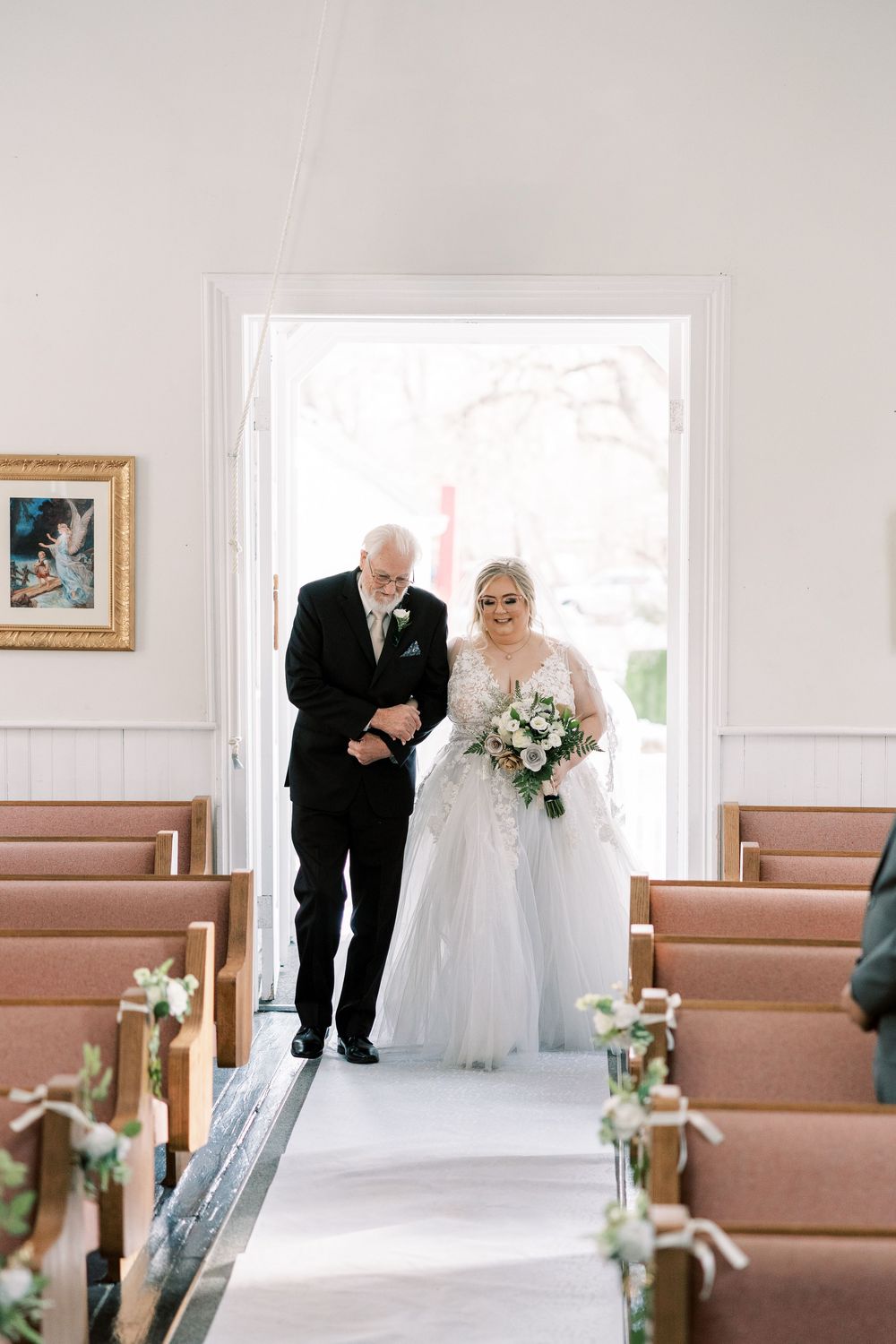 A wedding ceremony setup in a bright chapel with wooden pews decorated with floral arrangements along the aisle.