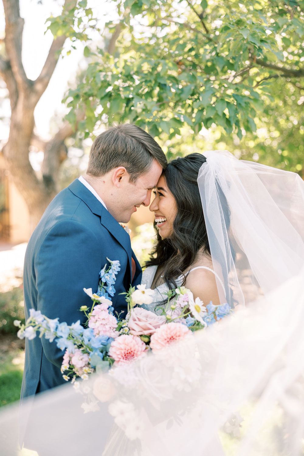 Romantic wedding couple embracing outdoors with soft pink and blue floral arrangements.