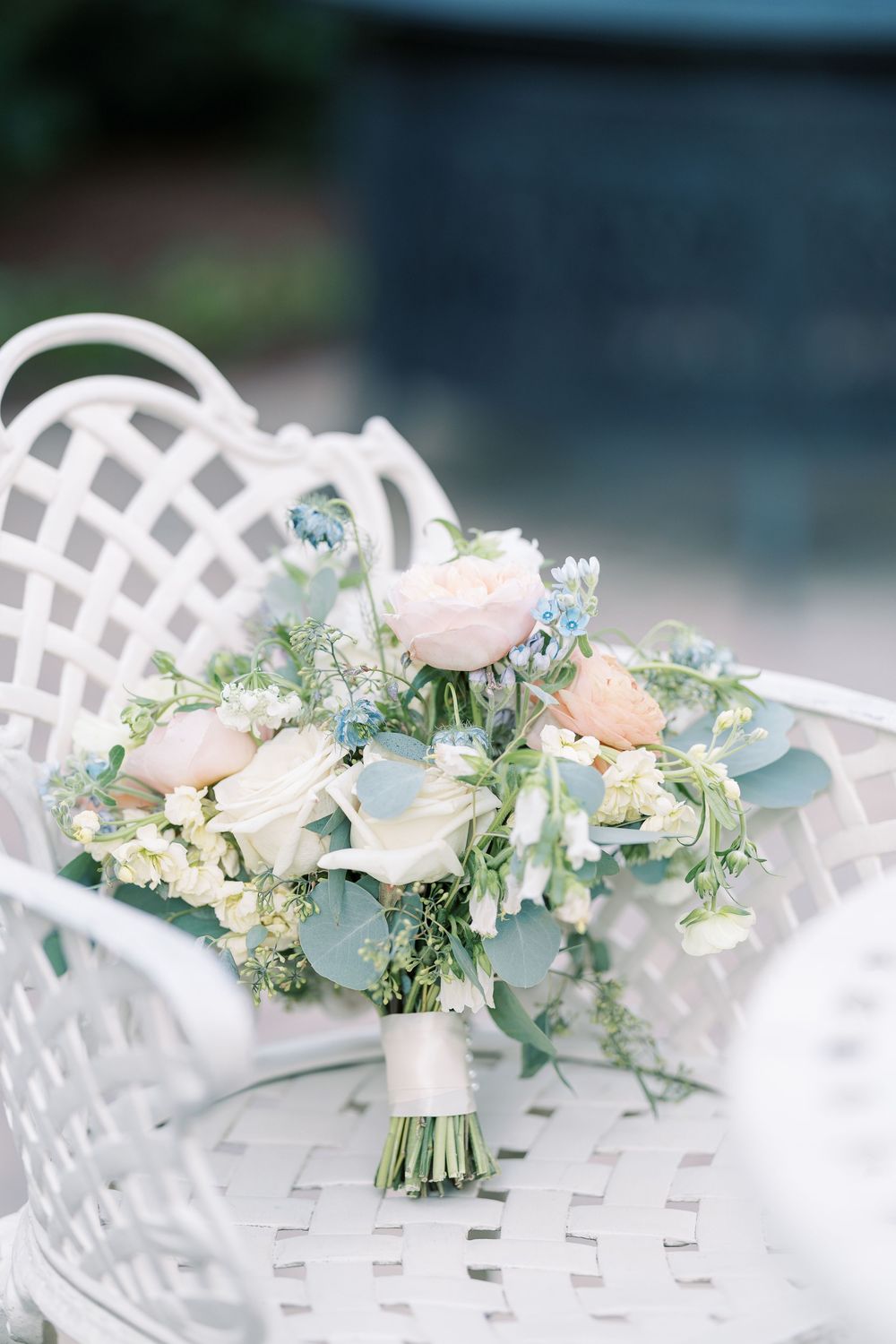 Delicate pastel floral arrangements with eucalyptus on white lattice chairs for an outdoor wedding.