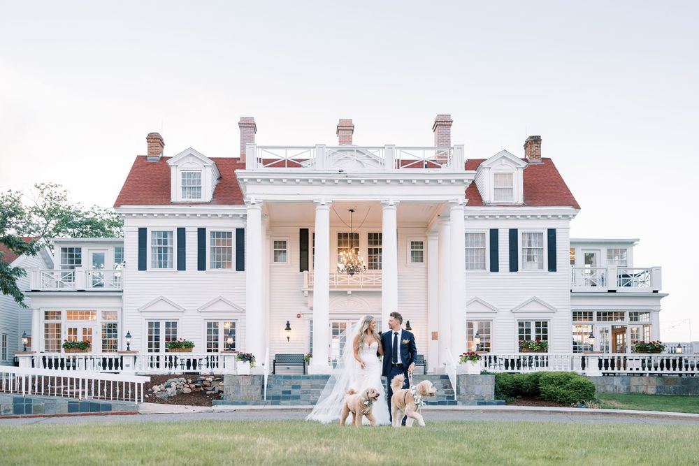 Elegant white colonial mansion with symmetrical columns serves as backdrop for wedding portraits.