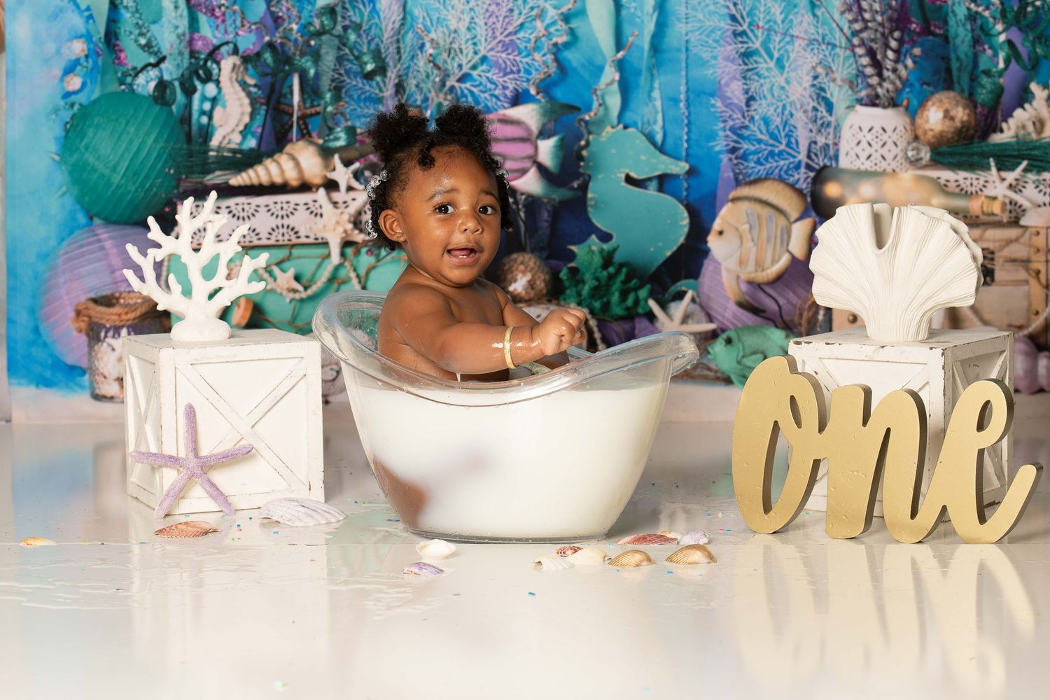 A small child sits in a white bathtub with an underwater themed backdrop featuring seahorses and coral decorations.