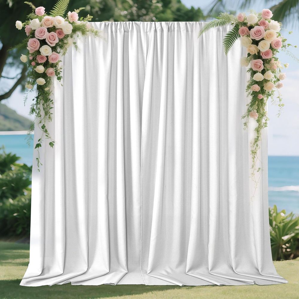 White fabric backdrop with pink and white floral arrangements creating an elegant wedding arch against an oceanfront setting.