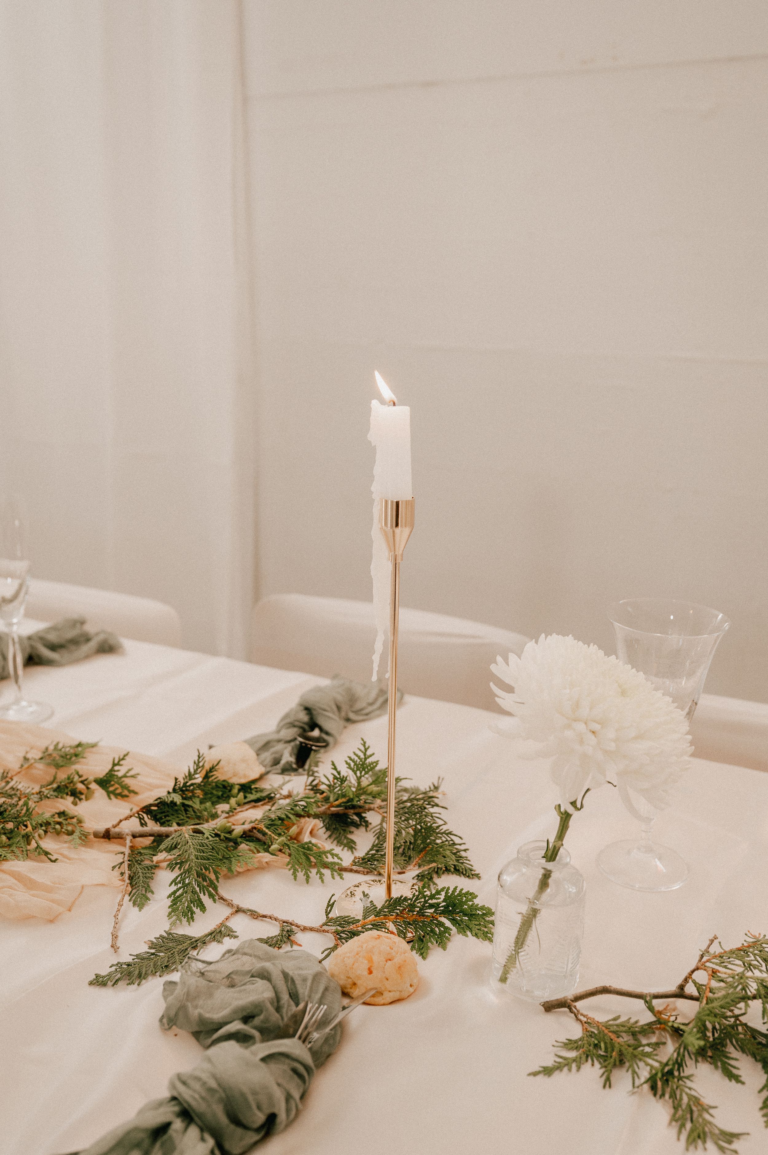 Elegant white candles and pine branches create a minimalist winter table decoration with soft neutral tones.