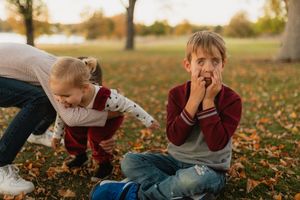 Two children playing in fallen autumn leaves on the ground during a golden sunset.