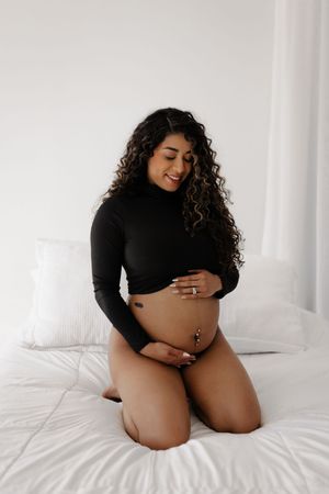 Black and white maternity boudoir photos showing woman in black top on white bedding.