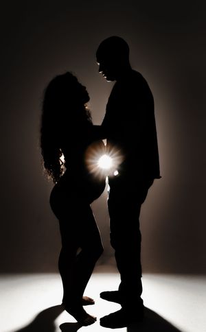 Two figures in dramatic silhouette against a bright light source create a romantic and moody atmosphere with their close poses.