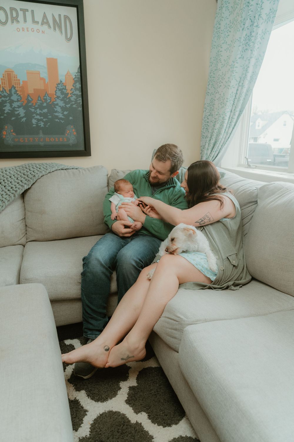 New parents sitting on a gray couch together admiring their newborn baby at home.