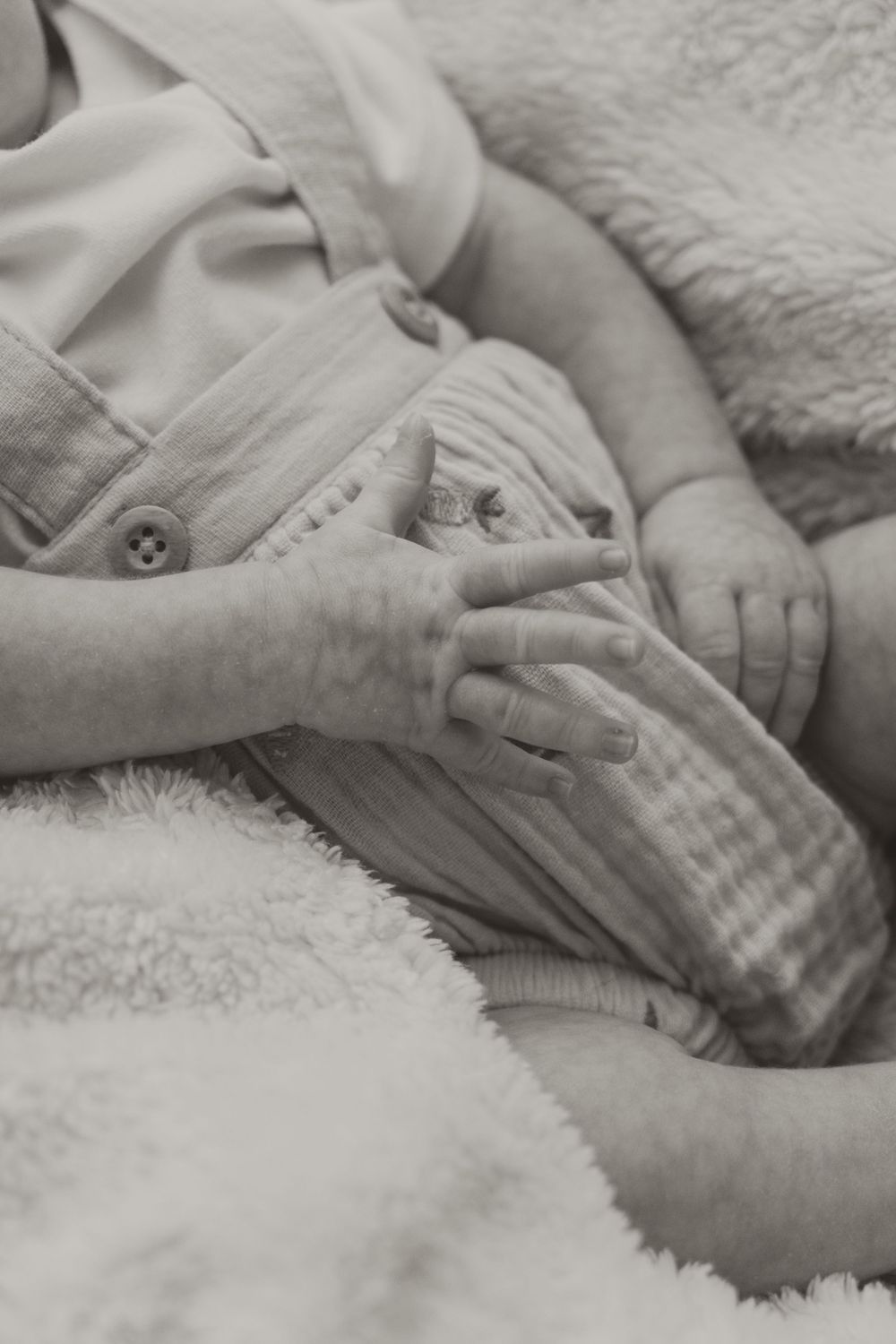 Black and white close-up of a newborn baby's tiny hands resting on a soft blanket.