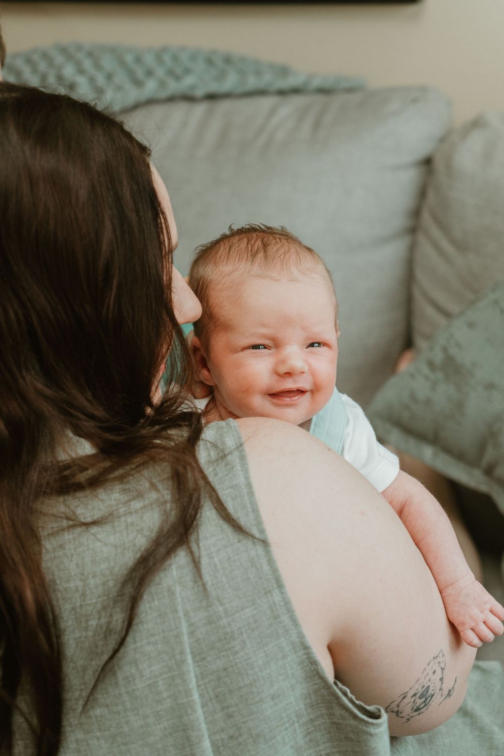 Newborn baby smiling over mother's shoulder while being held against her chest.