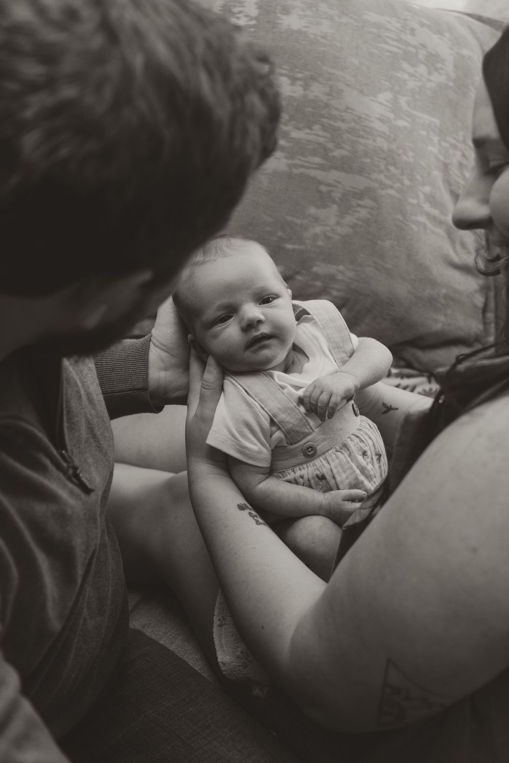 Black and white photo of parents gazing lovingly at their newborn baby between them.