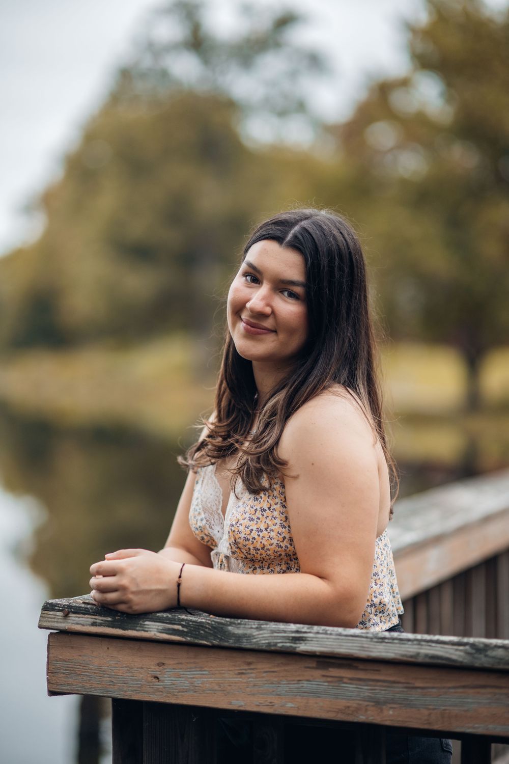 A person sits at a wooden railing in nature wearing a sequined top, photographed in soft outdoor lighting.