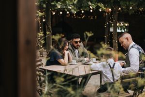 People dining at a rustic outdoor table under string lights in a garden setting.