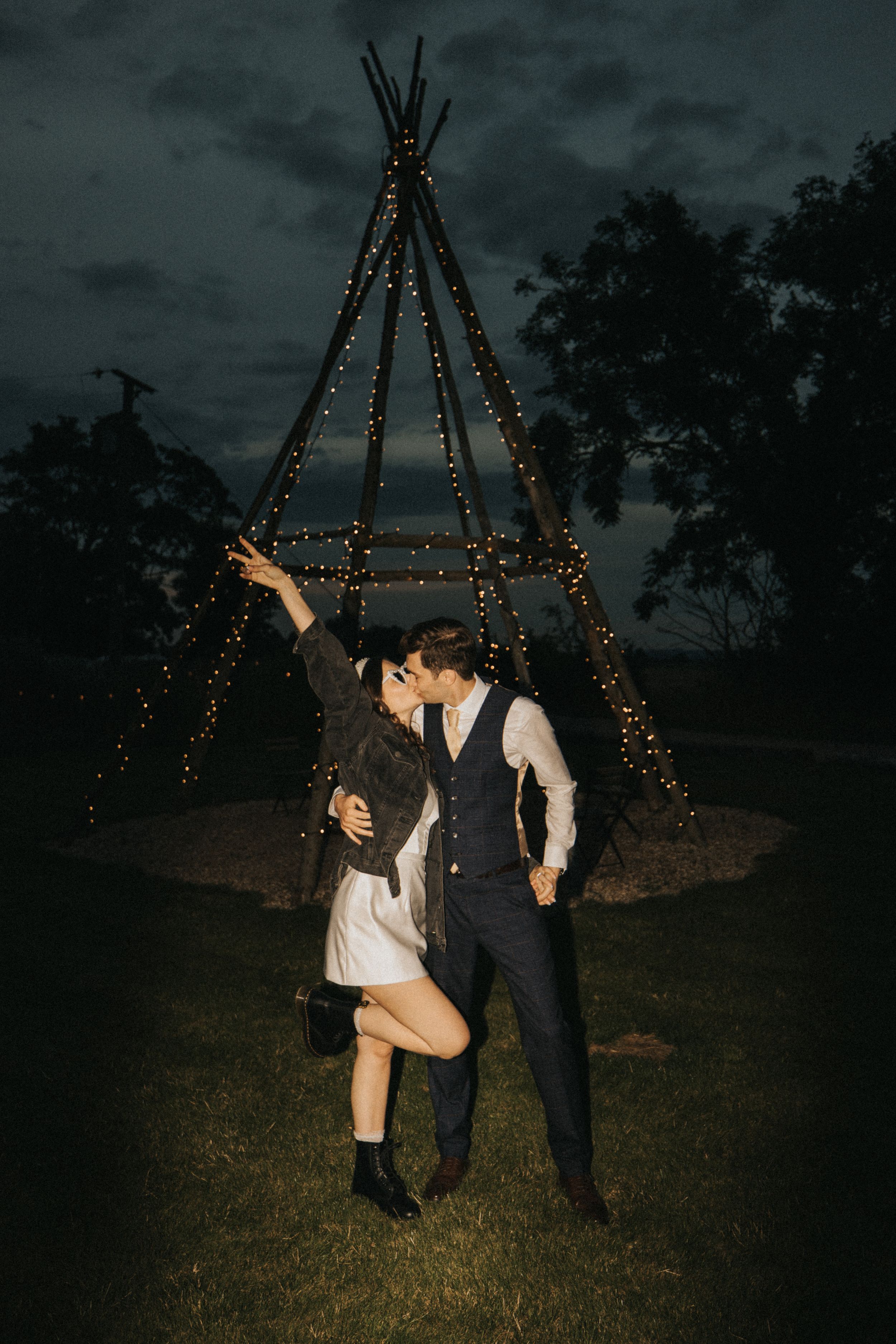 A romantic photo sequence at dusk featuring a couple near glowing teepee structures decorated with string lights.