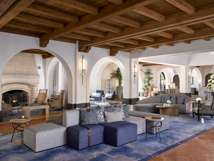Interior of a bright Mediterranean hotel lobby with exposed wooden beams and elegant archways connecting open living spaces.