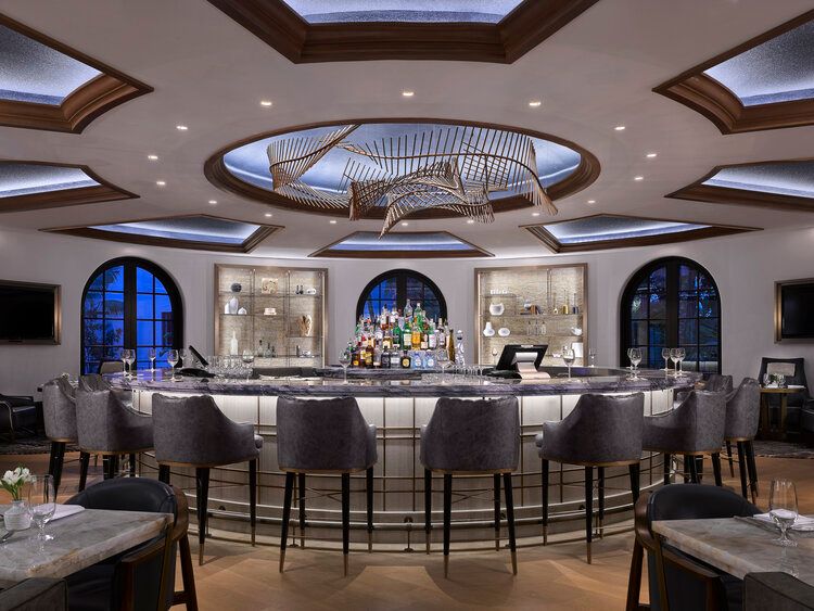Elegant circular bar with plush gray seating, skylights, and arched windows in an upscale restaurant interior.