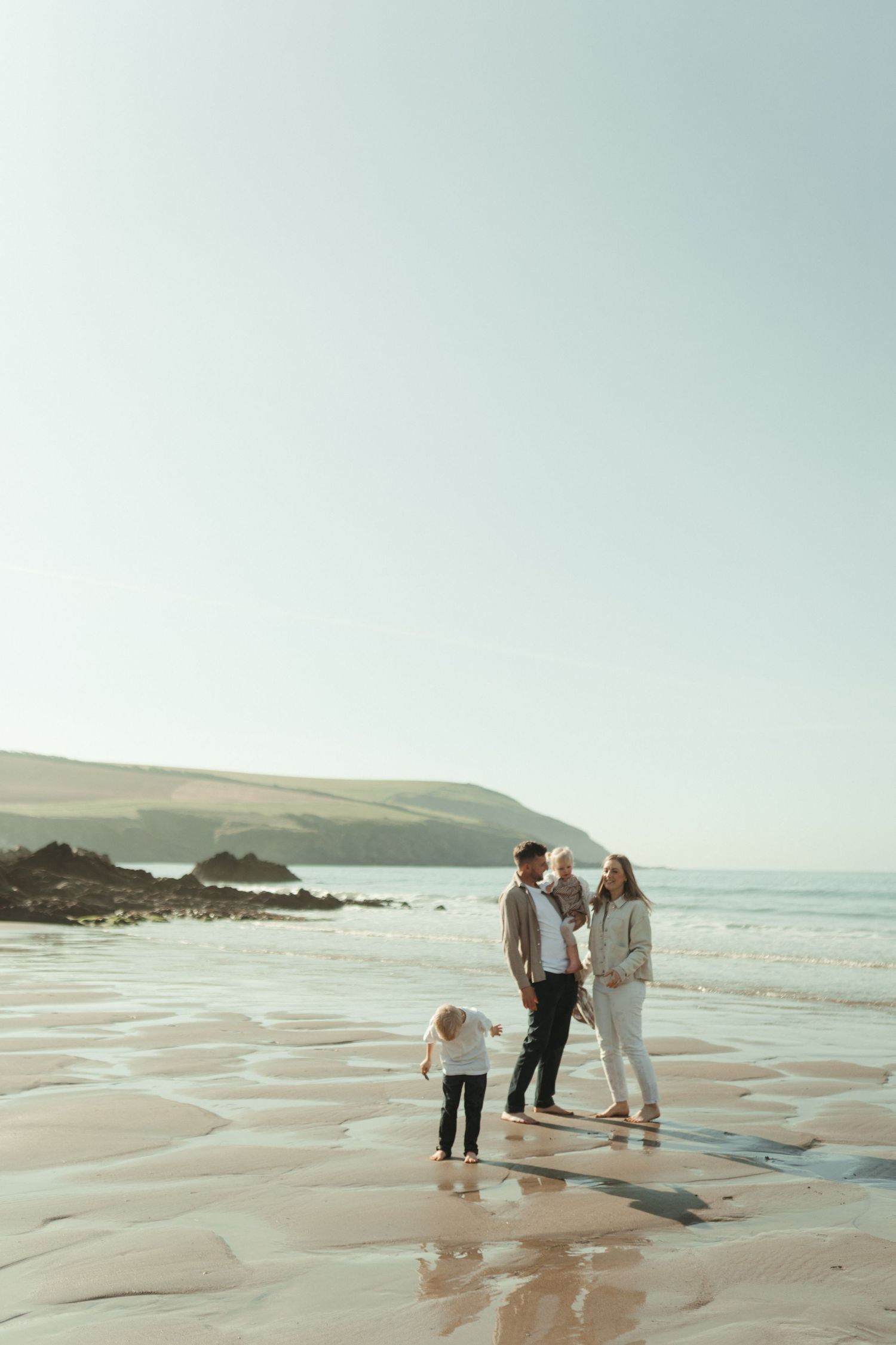 A family enjoys a peaceful moment together walking along a rocky beach at sunset with cliffs in the background.