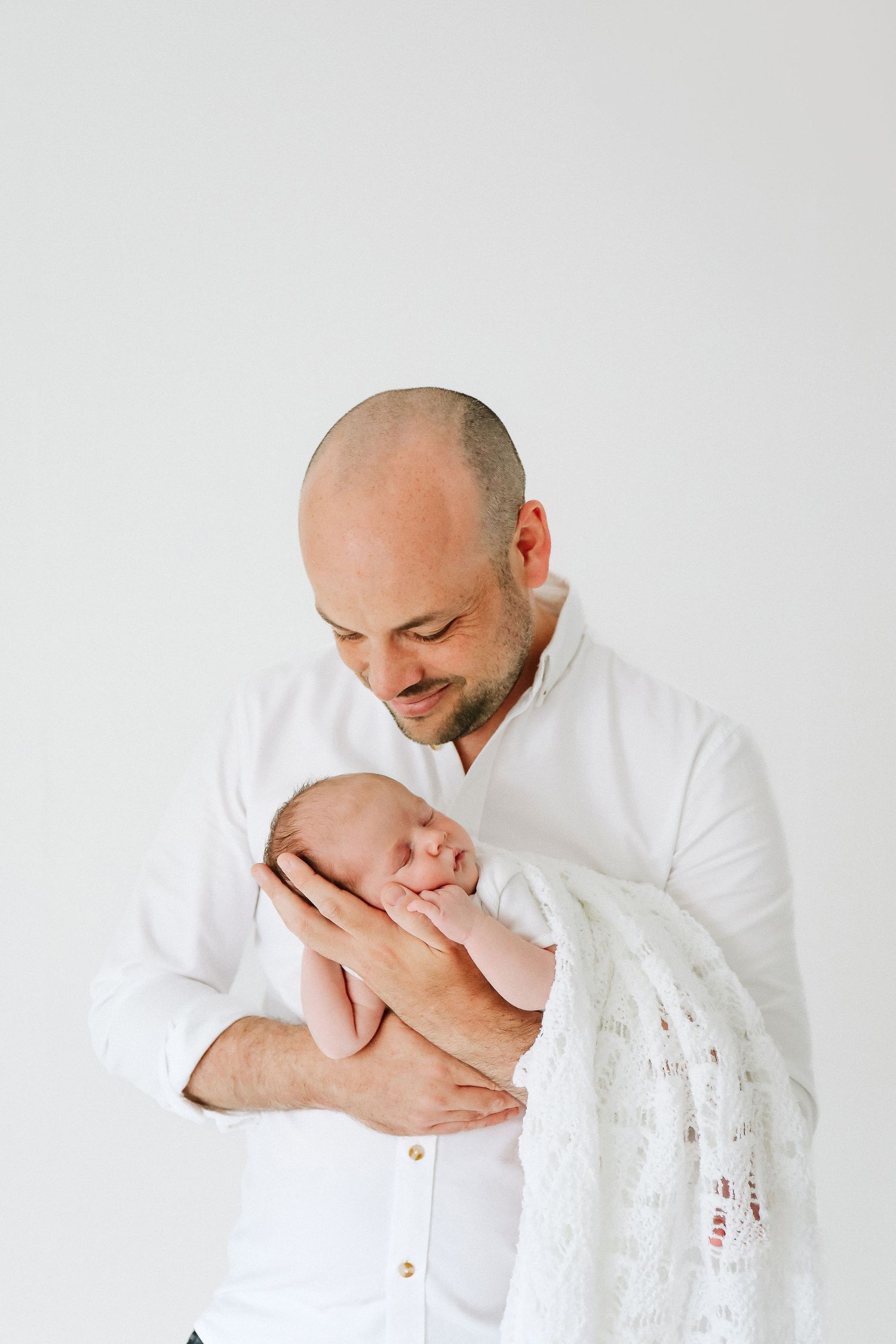 A tender moment captures a dad cradling his sleeping newborn wrapped in delicate lace blanket, during newborn photoshoot in Nottingham