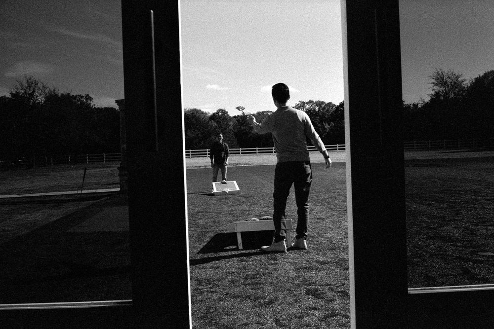 Black and white photo of two people playing catch on an open field viewed through glass doors.