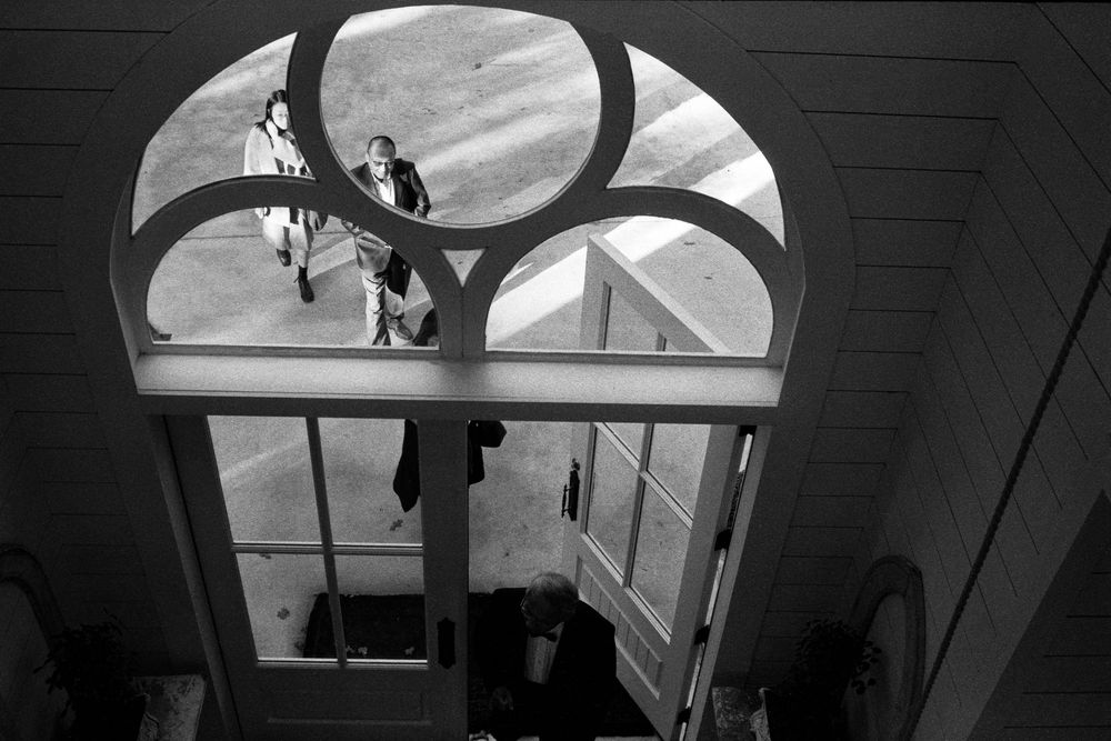 Black and white aerial view of two people entering a church through ornate arched doors before a wedding.