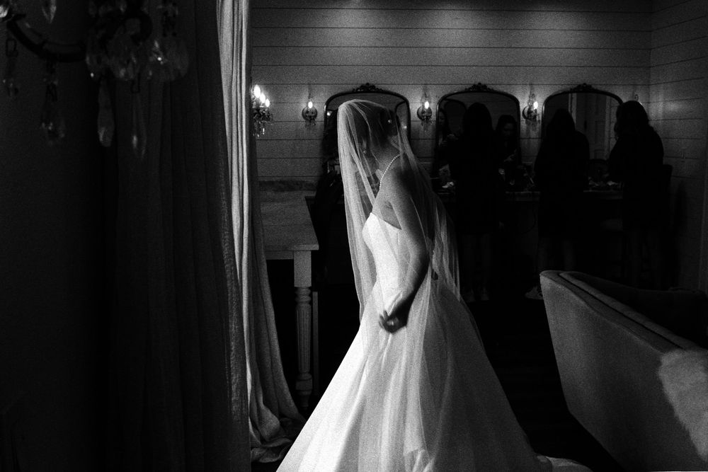 Black and white silhouette of bride in wedding gown and veil standing indoors.