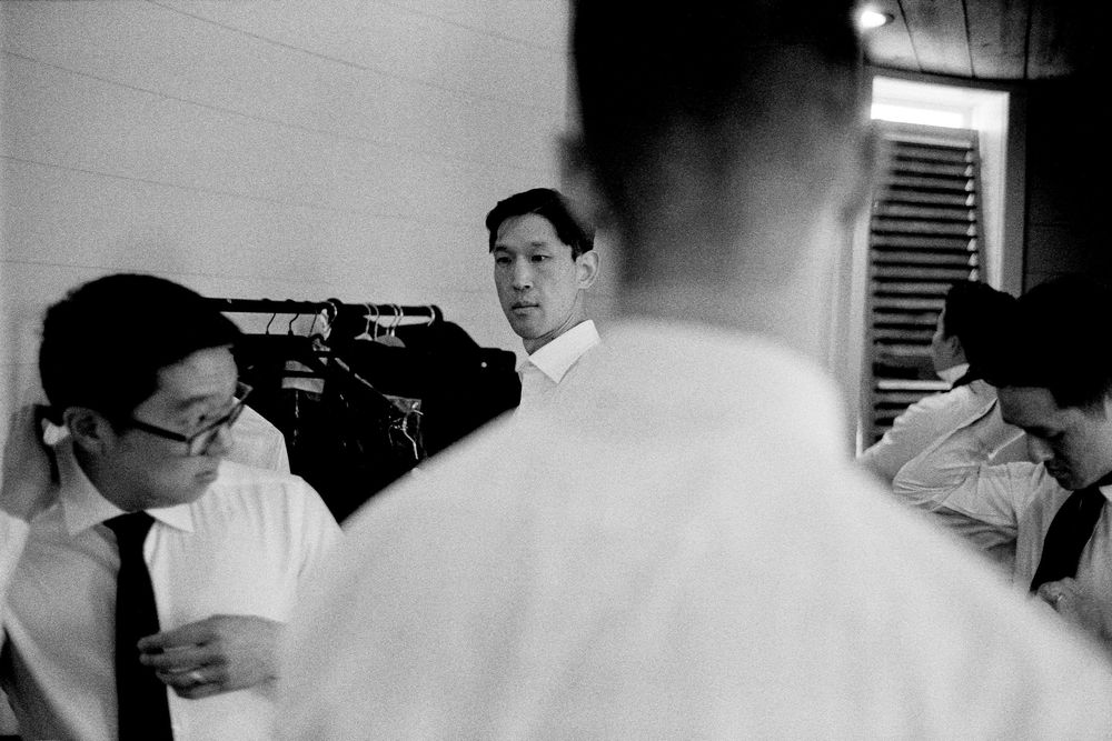 Black and white candid photo of groomsmen in white shirts and ties preparing for a wedding.
