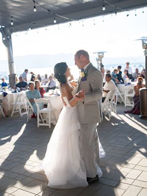 A couple sharing a romantic dance during what appears to be a light-filled reception venue by the waterfront.