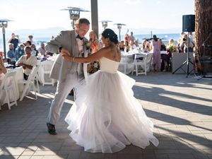 A dancing couple share an elegant moment on an outdoor dance floor at a wedding reception by the beach.