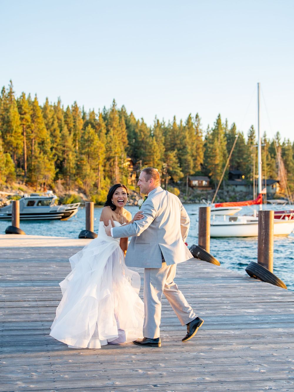 A couple shares a romantic sequence of dance moves on a wooden dock by a lake during golden hour.