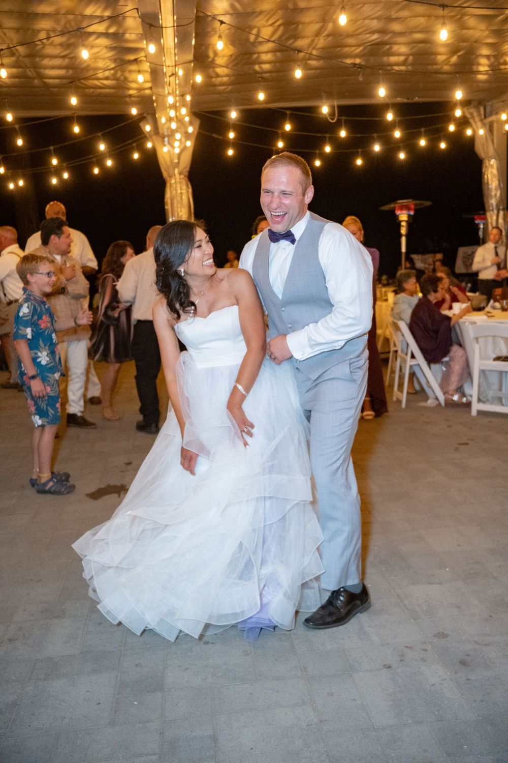 A couple dances in festive celebration under warm string lights in a rustic barn venue.