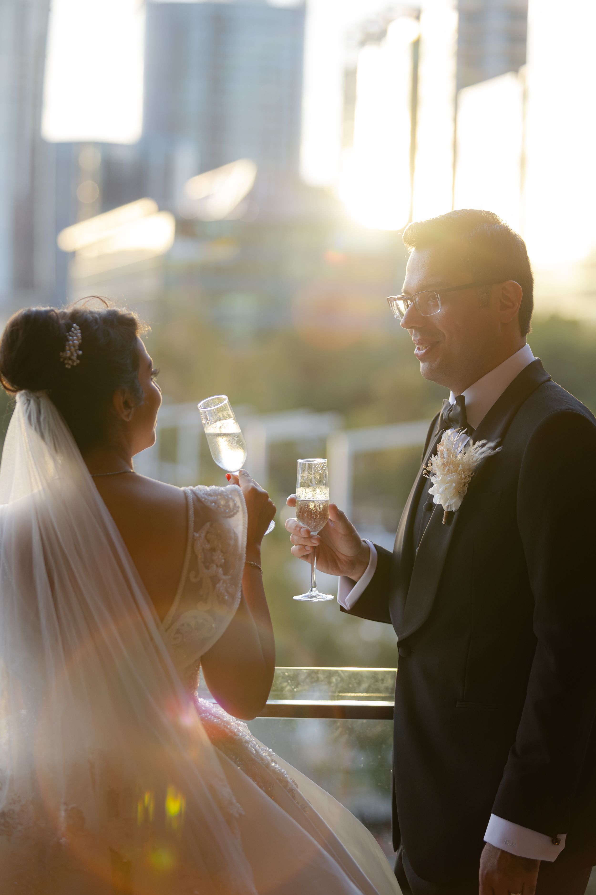 A bride and groom raise champagne glasses during a wedding toast at sunset by the water.