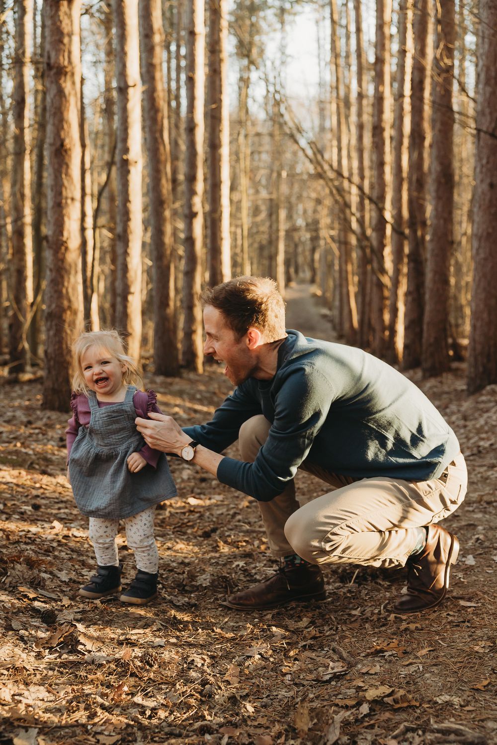 A joyful moment in a sunny autumn forest with an adult and small child playing together among tall pine trees.