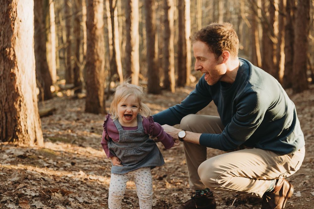 A family relaxes together in an autumn forest during golden hour as sunlight filters through tall trees.