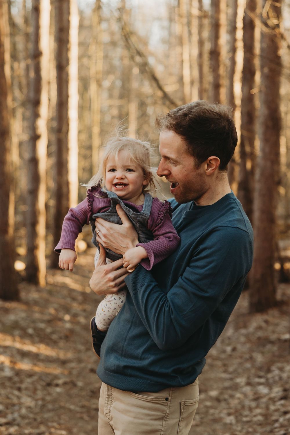 Candid moment of parent and child laughing together while walking through an autumn forest.