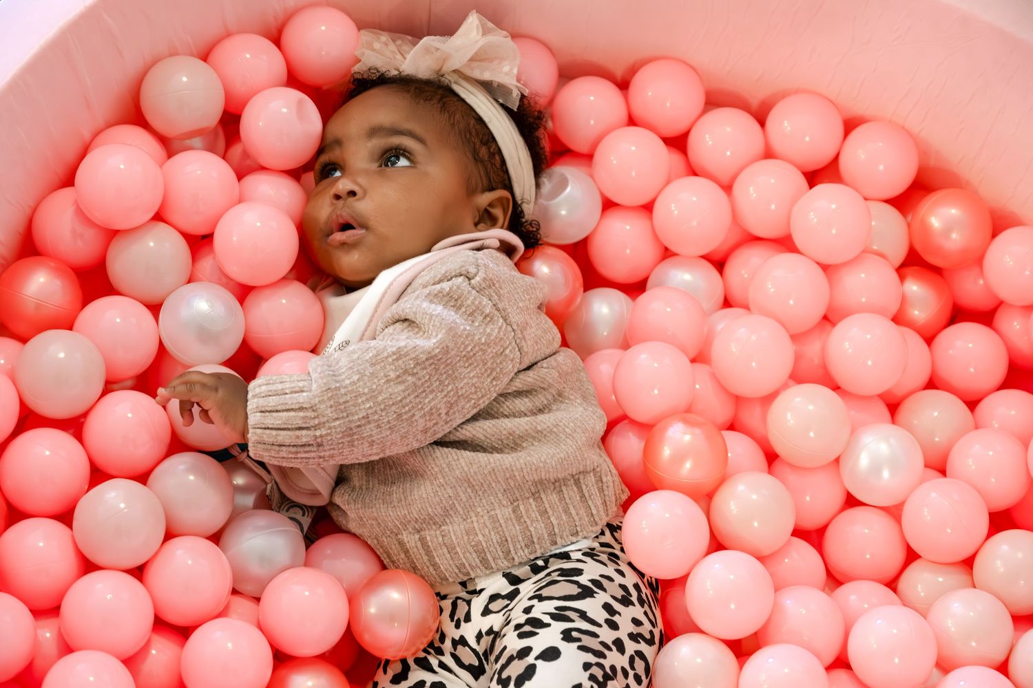 Children jumping and playing with orange and white balloons in a brightly lit white room during a birthday celebration.