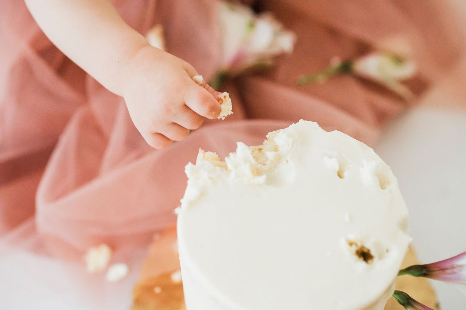 Baby in pink tulle dress crawls and smiles playfully on white backdrop with delicate floral accents in studio setting.