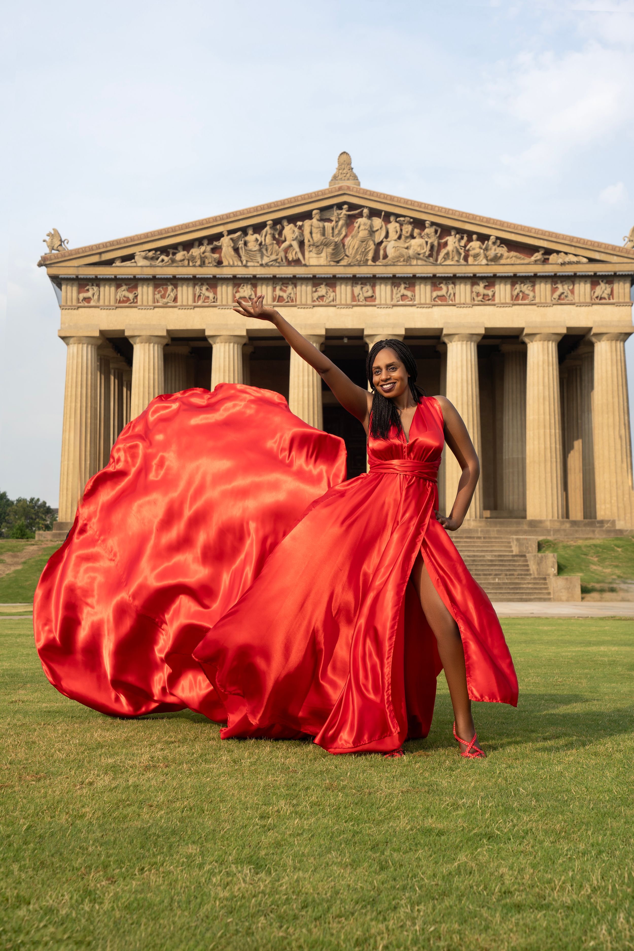 A flowing red gown flows dramatically in front of the Nashville Parthenon replica creating an artistic fashion photograph.